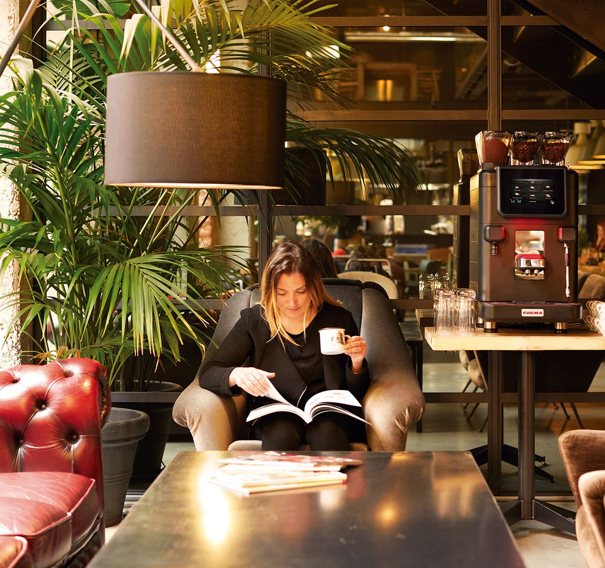 Donna seduta in caffetteria con macchina da caffè Faema sullo sfondo